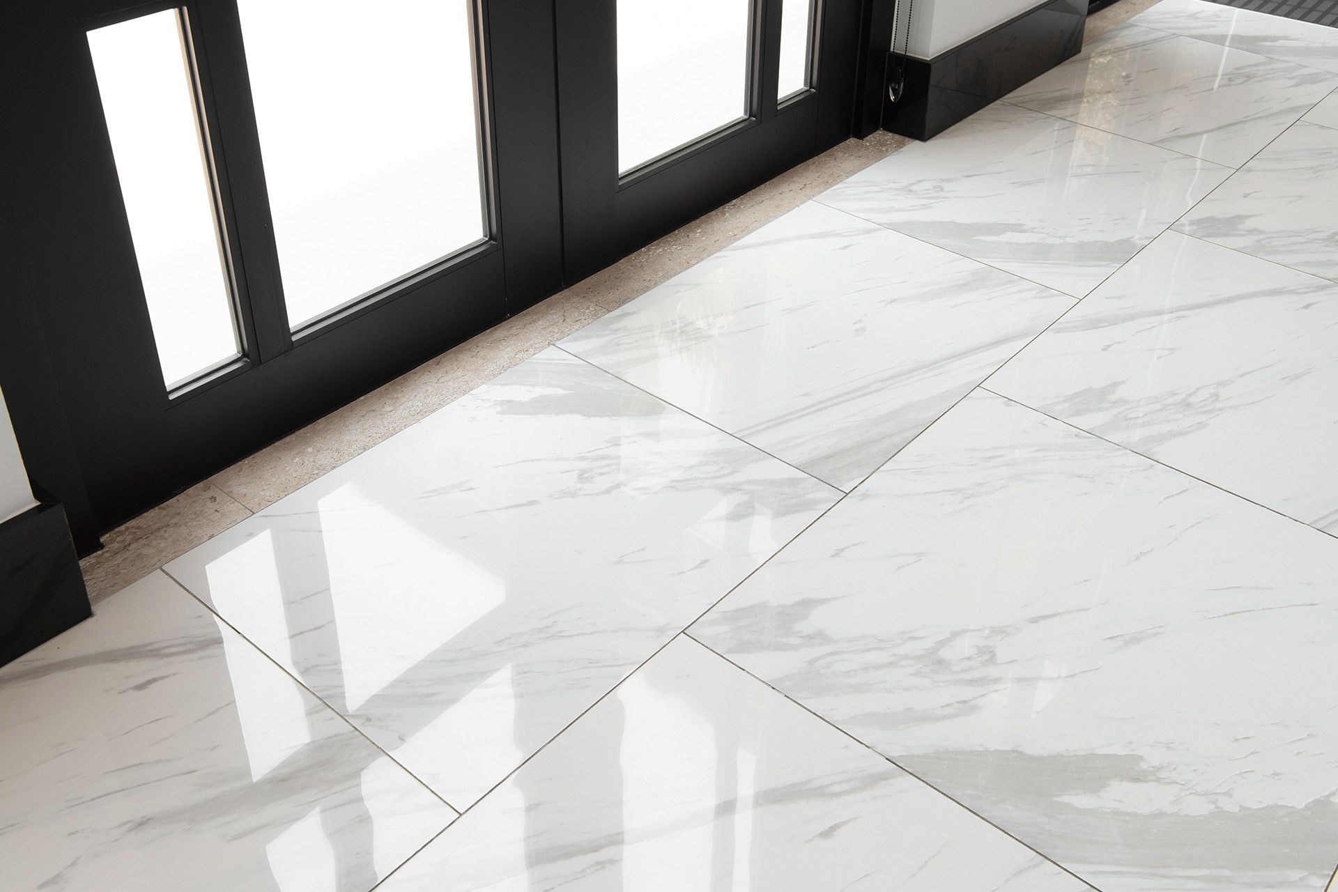 Glossy white marble tile floor beside black-framed glass doors in a bright interior