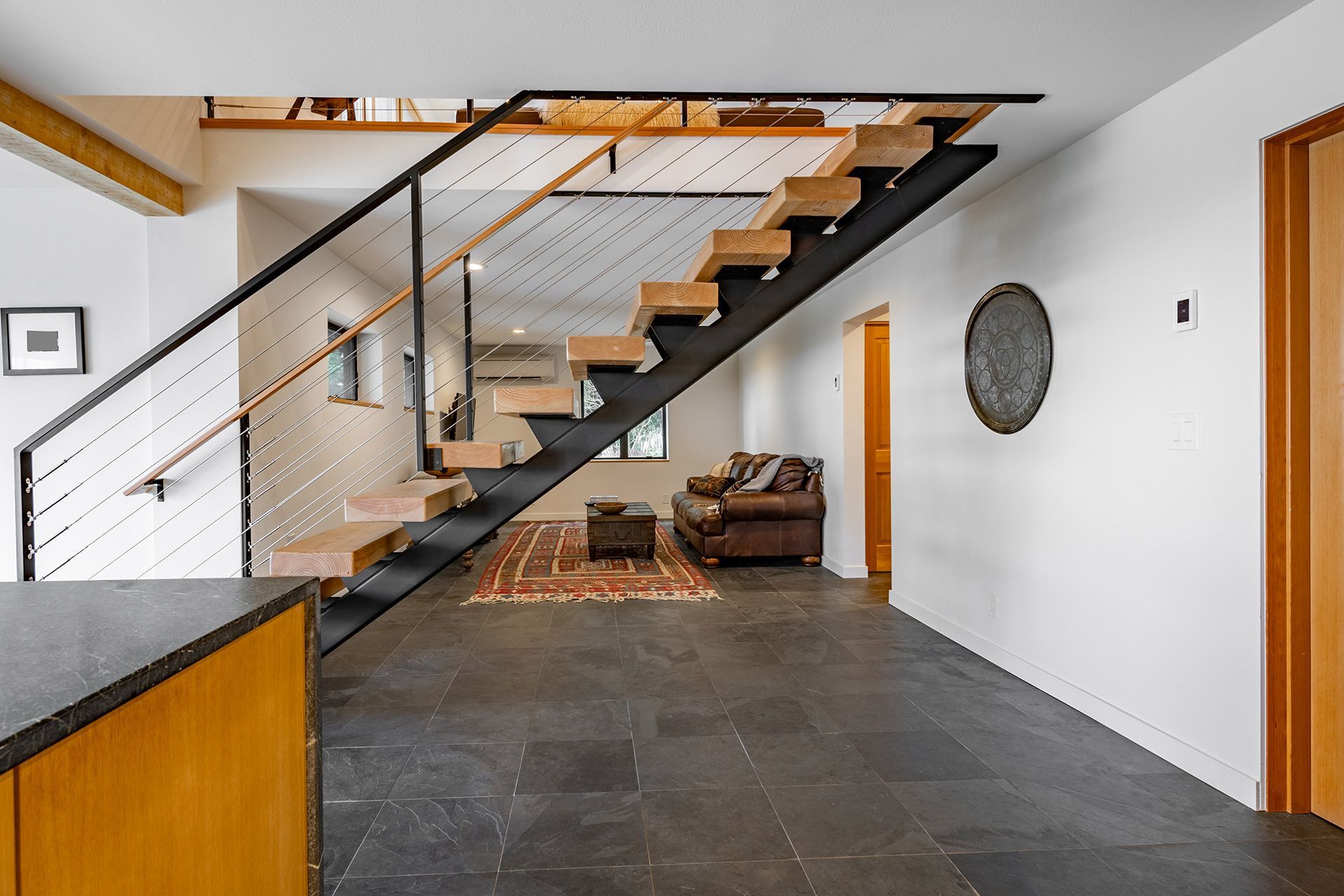 Modern open-plan interior with floating staircase, dark tile floor, and leather chair