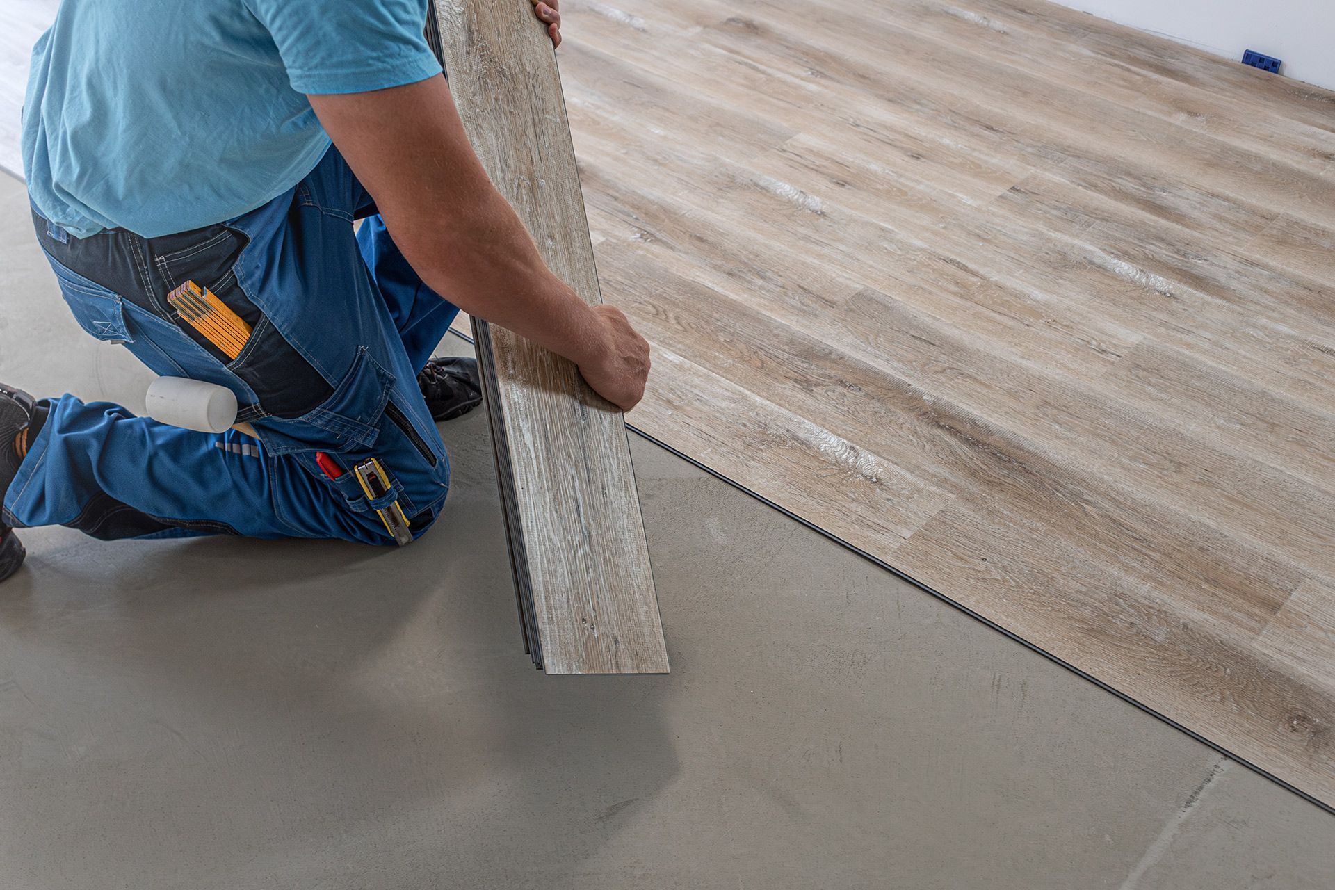 Worker laying wood-look flooring over a gray subfloor.