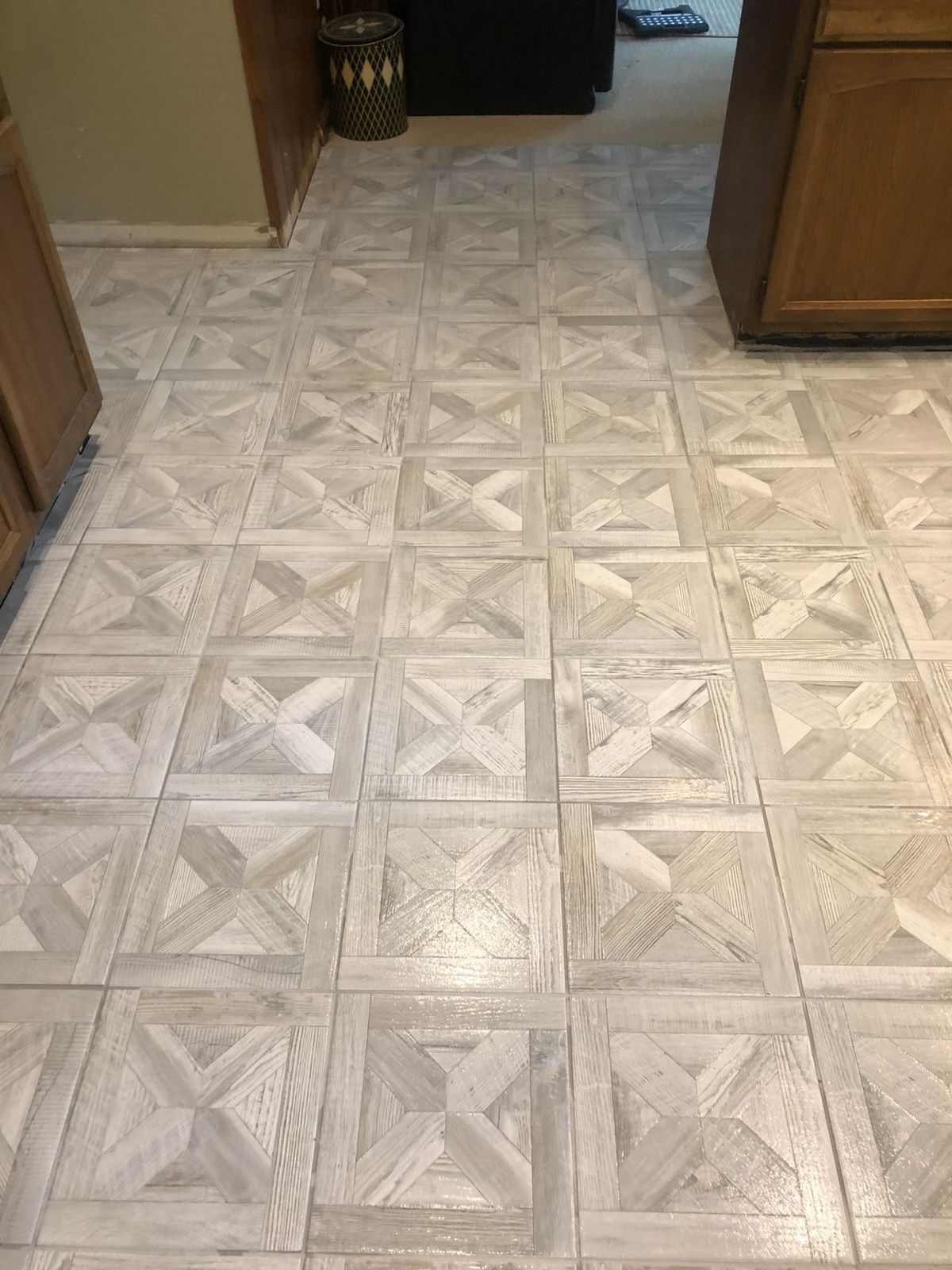 Patterned beige tile floor in a hallway between wooden cabinets and a doorway