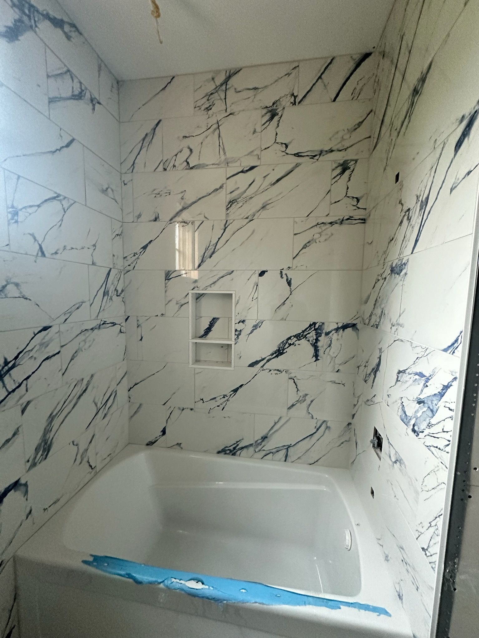 Marble-look tiled bathtub alcove with built-in wall niches and a window above the tub