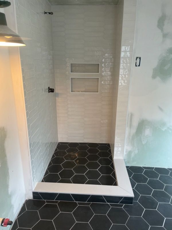 Small shower stall with white subway tiles, black hexagon floor, and a recessed wall niche.