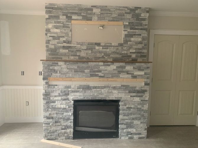 Living room stone fireplace with mantel and TV mount, flanked by white built-in cabinets and a closed door