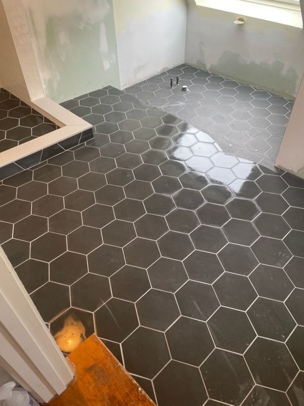 Small bathroom with dark hexagon tile floor, white walls, and a shower curb at left.