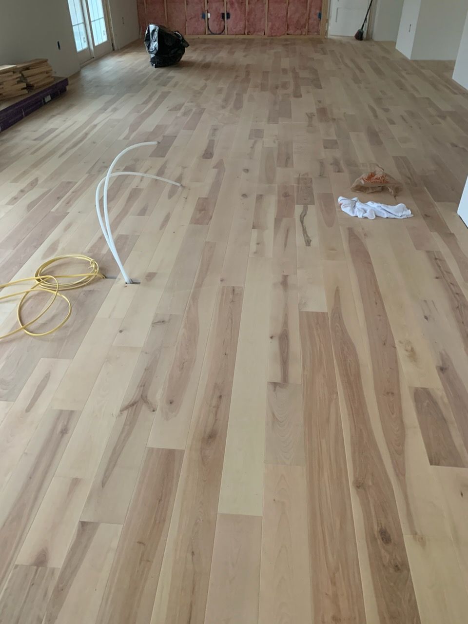 Empty room with light wood flooring, loose cables, and construction materials near the far wall.