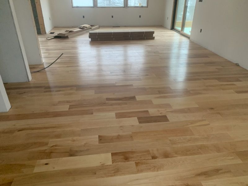 Empty room with light wood flooring and unfinished walls, with construction materials near the back.