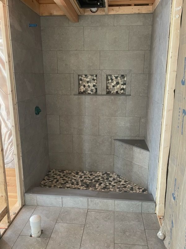 Partially tiled shower stall with gray walls, pebble floor, and recessed niches in a bathroom under construction