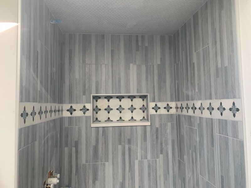 Empty gray-tiled shower with decorative white tile border and small accent panel.