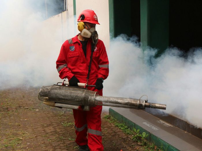 A professional in a jumpsuit is spraying pesticide from a machine.