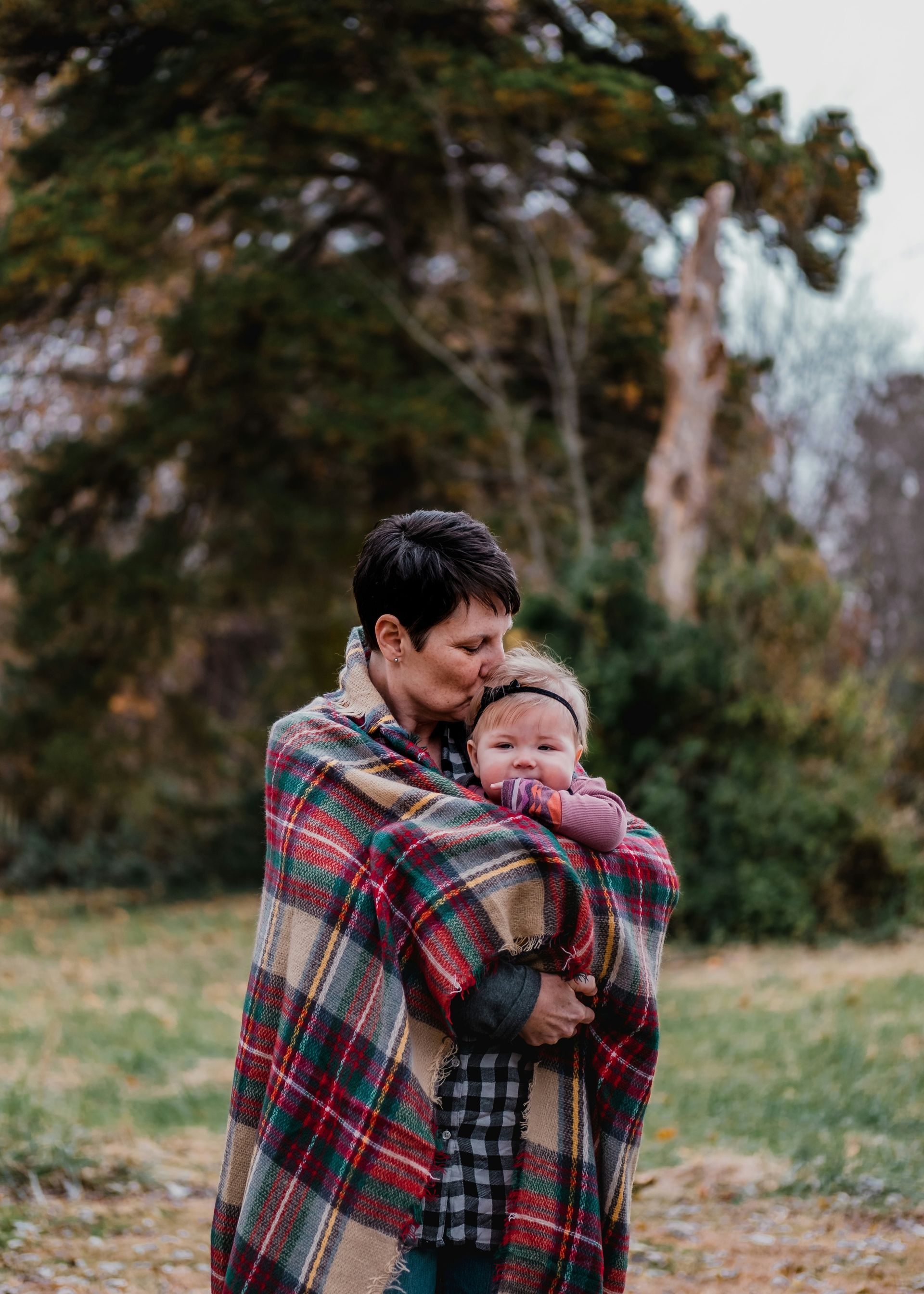 A woman is holding a baby wrapped in a plaid blanket.
