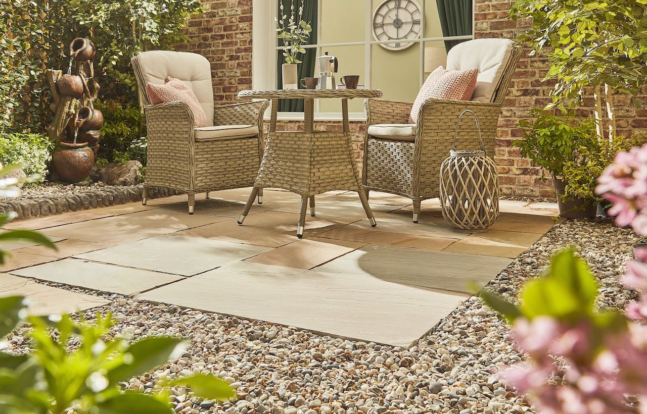 Patio with wicker furniture set on a stone patio surrounded by gravel and plants, under a sunny sky.