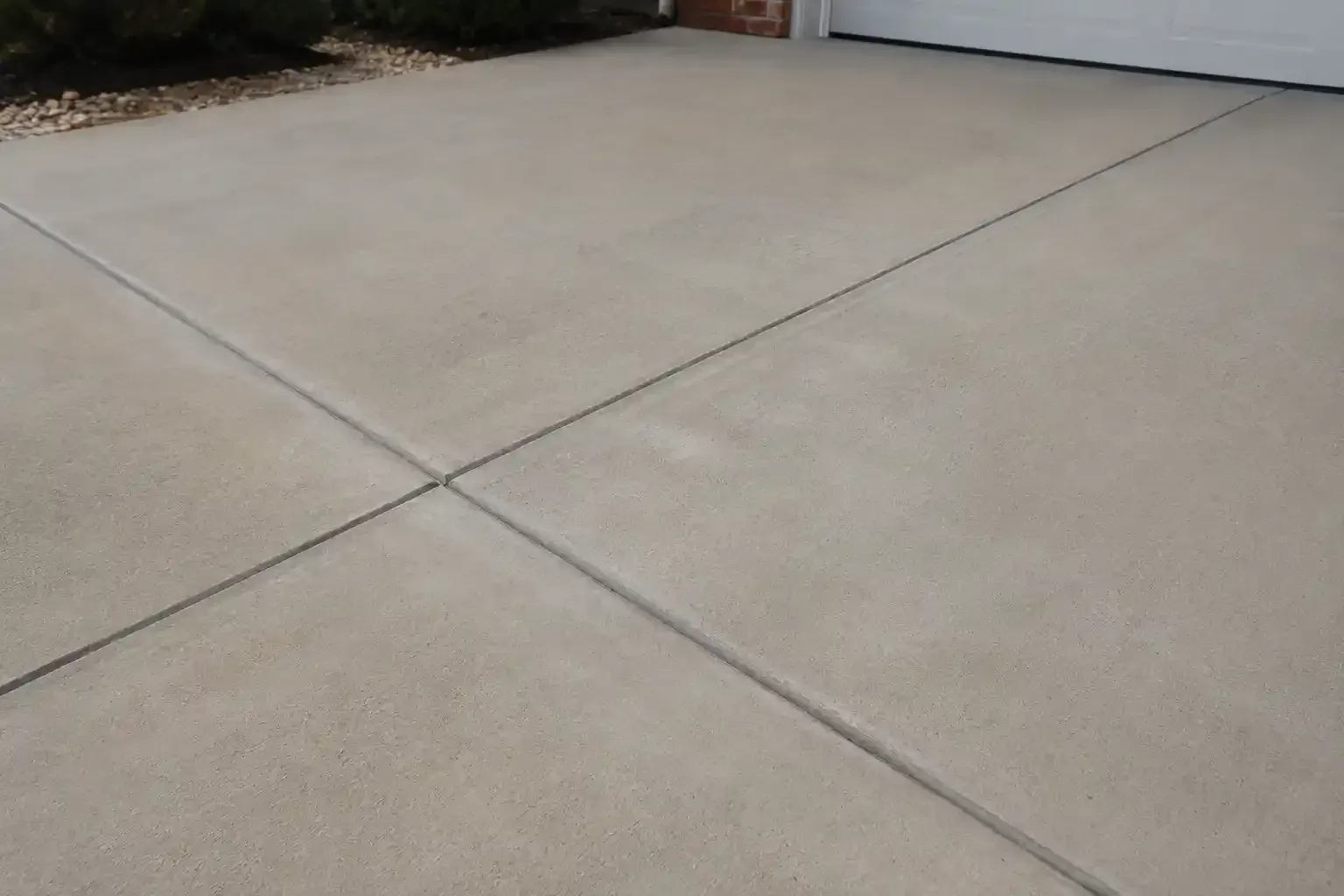 Concrete driveway with diagonal expansion joints and a small landscaped edge at the top left