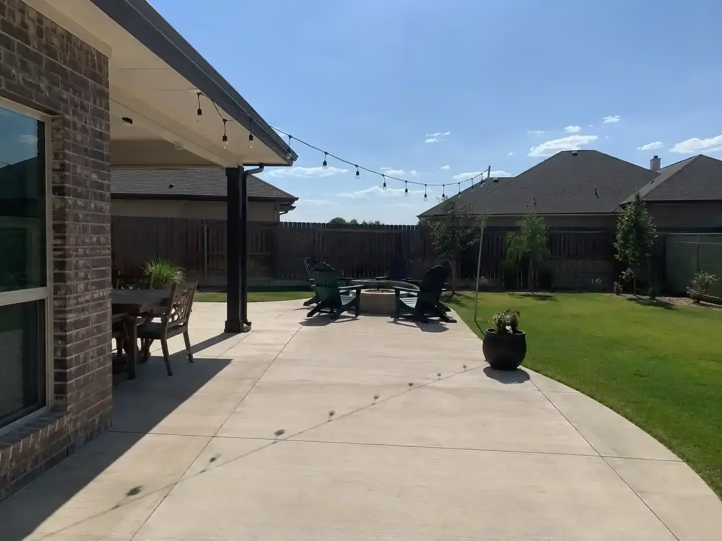 Back patio with concrete walkway, outdoor furniture, and green lawn beside a brick house.