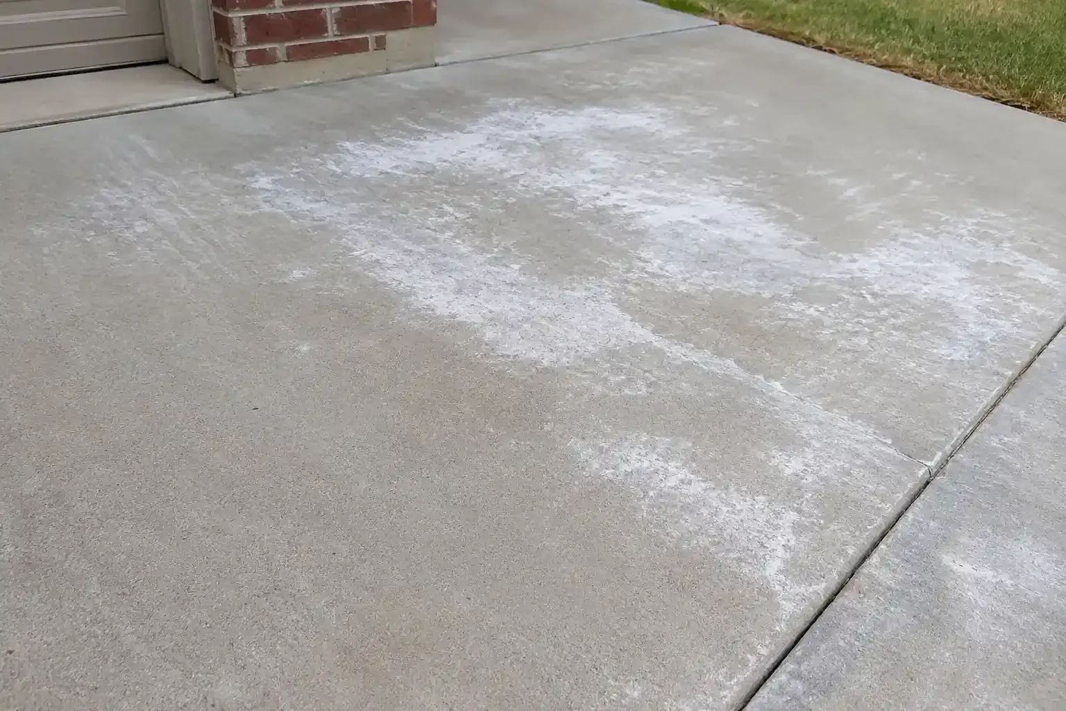 Efflorescence concrete driveway beside a brick wall and garage door