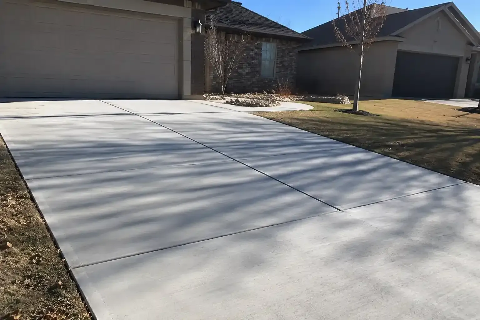 Freshly poured concrete driveway in front of a suburban house with garage doors