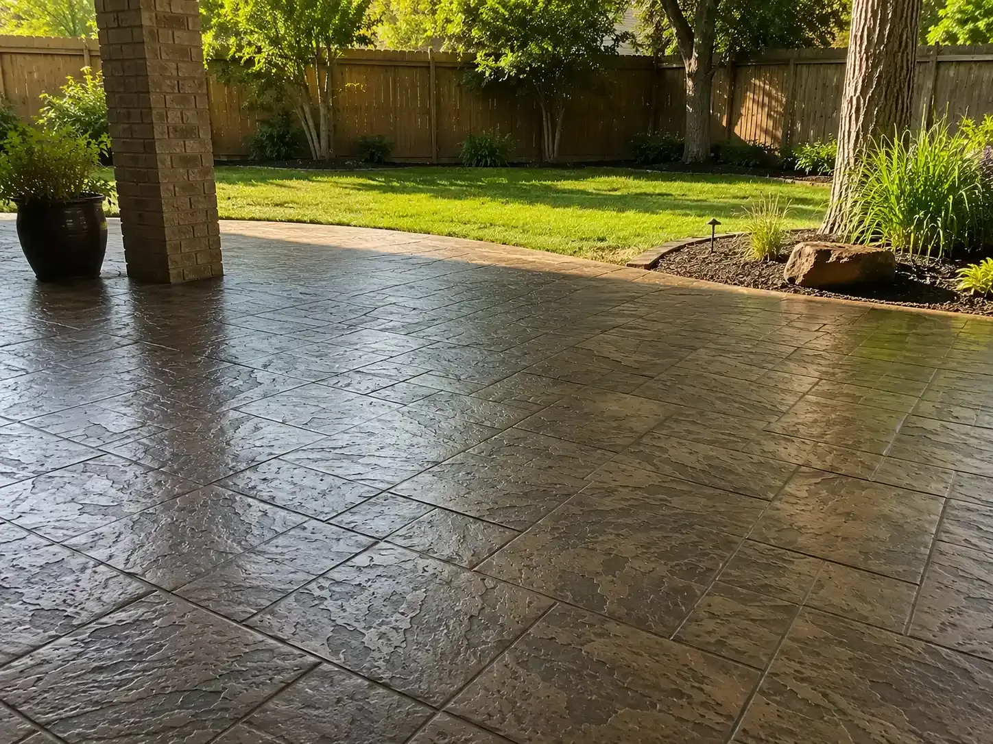 Stamped concrete patio under a covered area, opening to a sunny backyard with grass and trees.