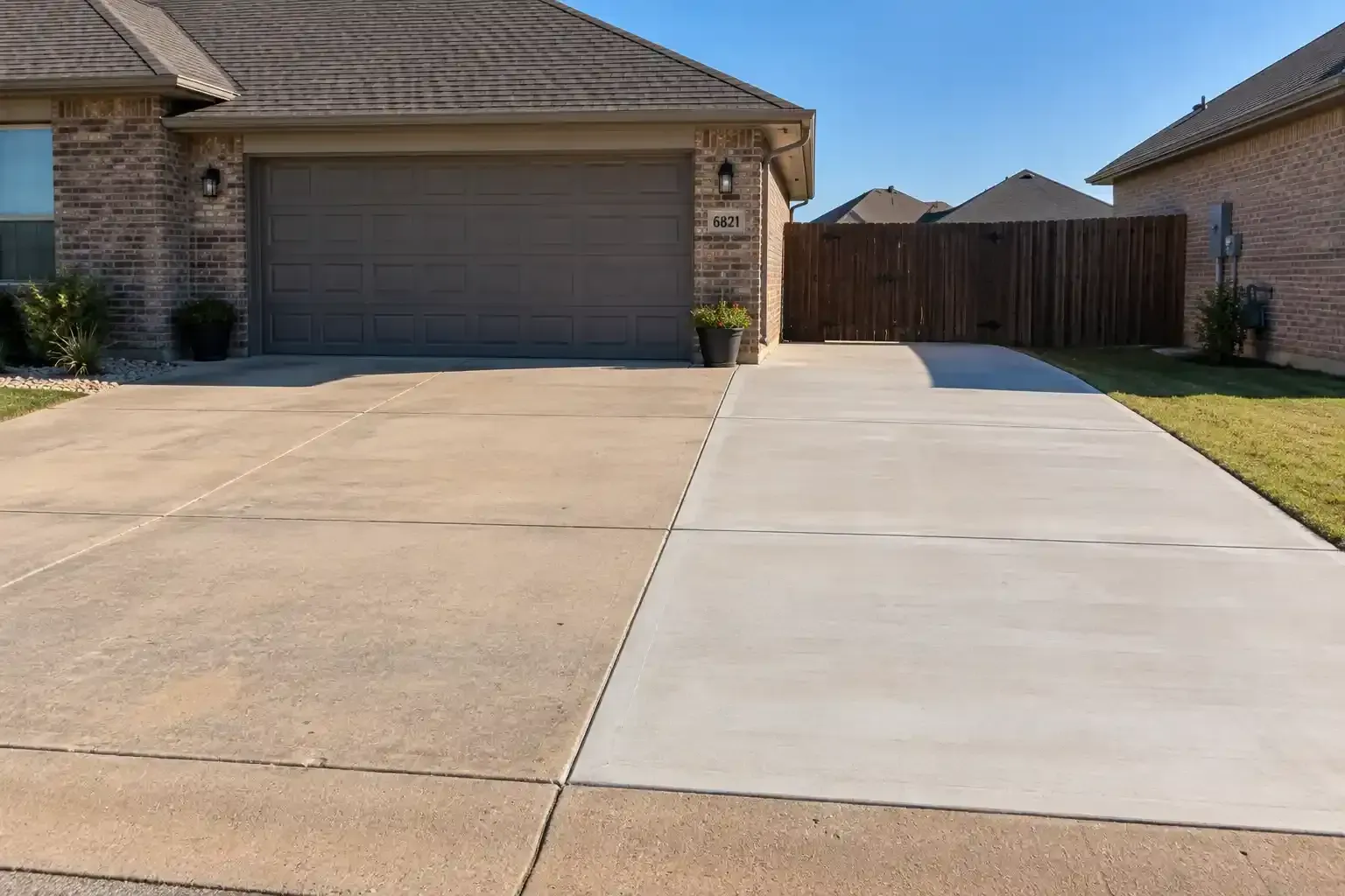 Suburban driveway with a garage and a wooden fence, split between old tan concrete and new light concrete slab