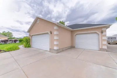 Two-car beige garage with white doors with a new wide concrete driveway under a cloudy sky