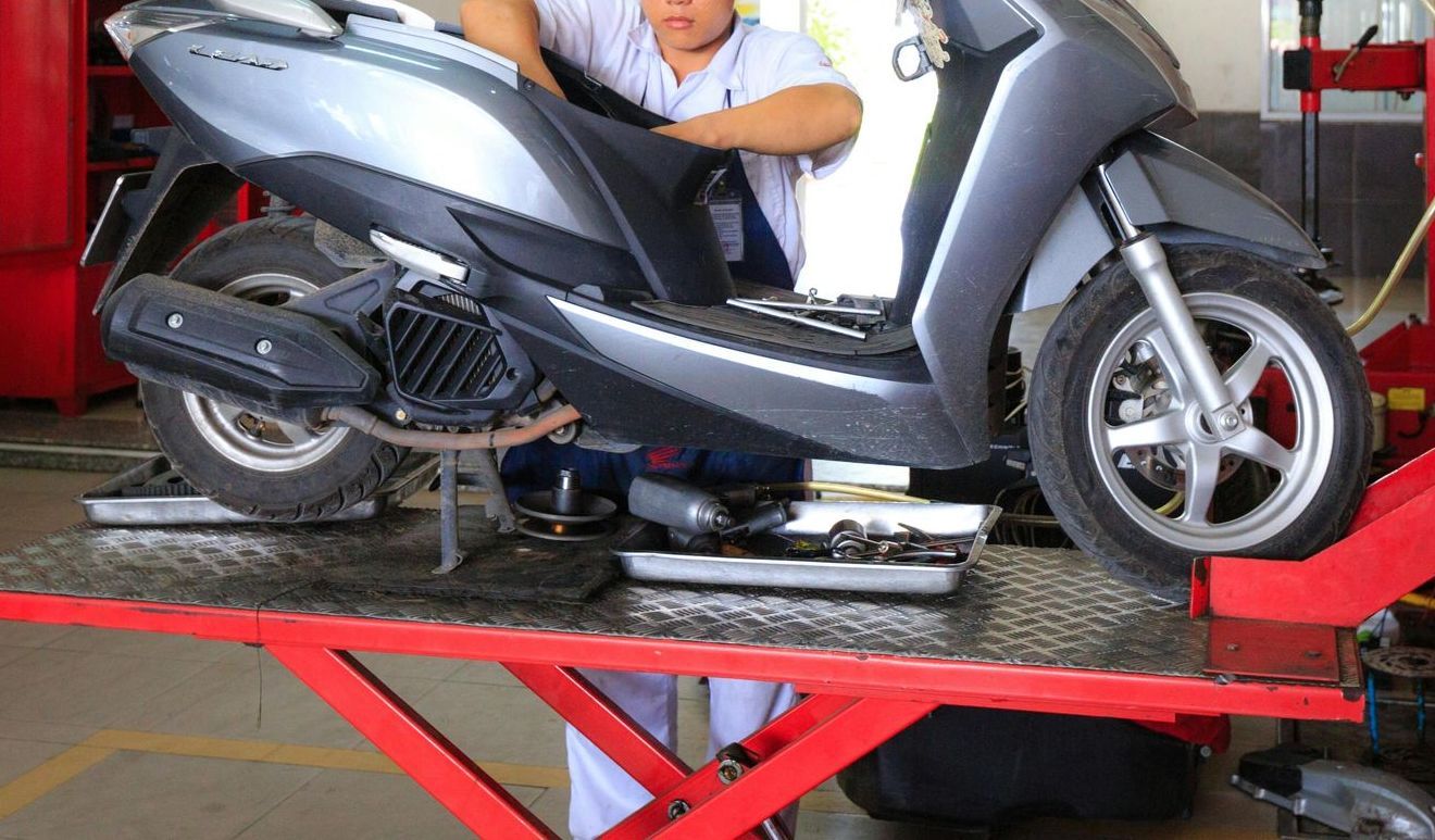 A man is working on a scooter on a lift in a garage.