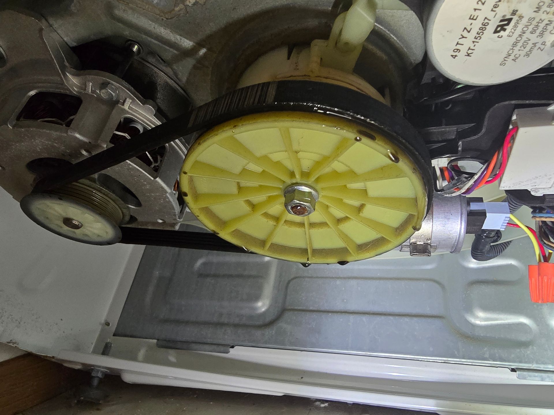 Inside a washing machine: yellow pulley with a black belt connected to a motor.