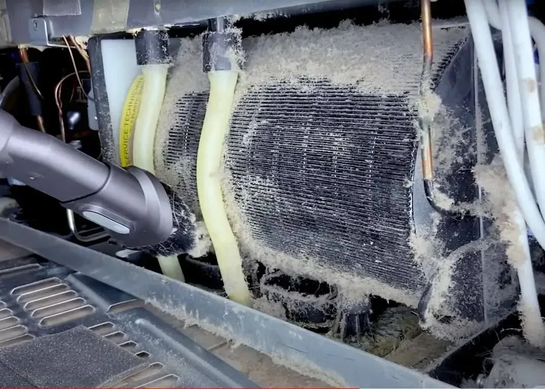 Vacuuming a dusty refrigerator condenser coils.