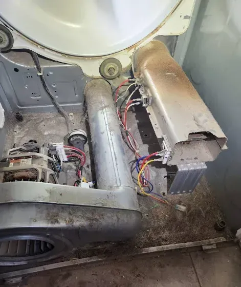 Inside of a dryer with various components exposed and covered in lint and dust.
