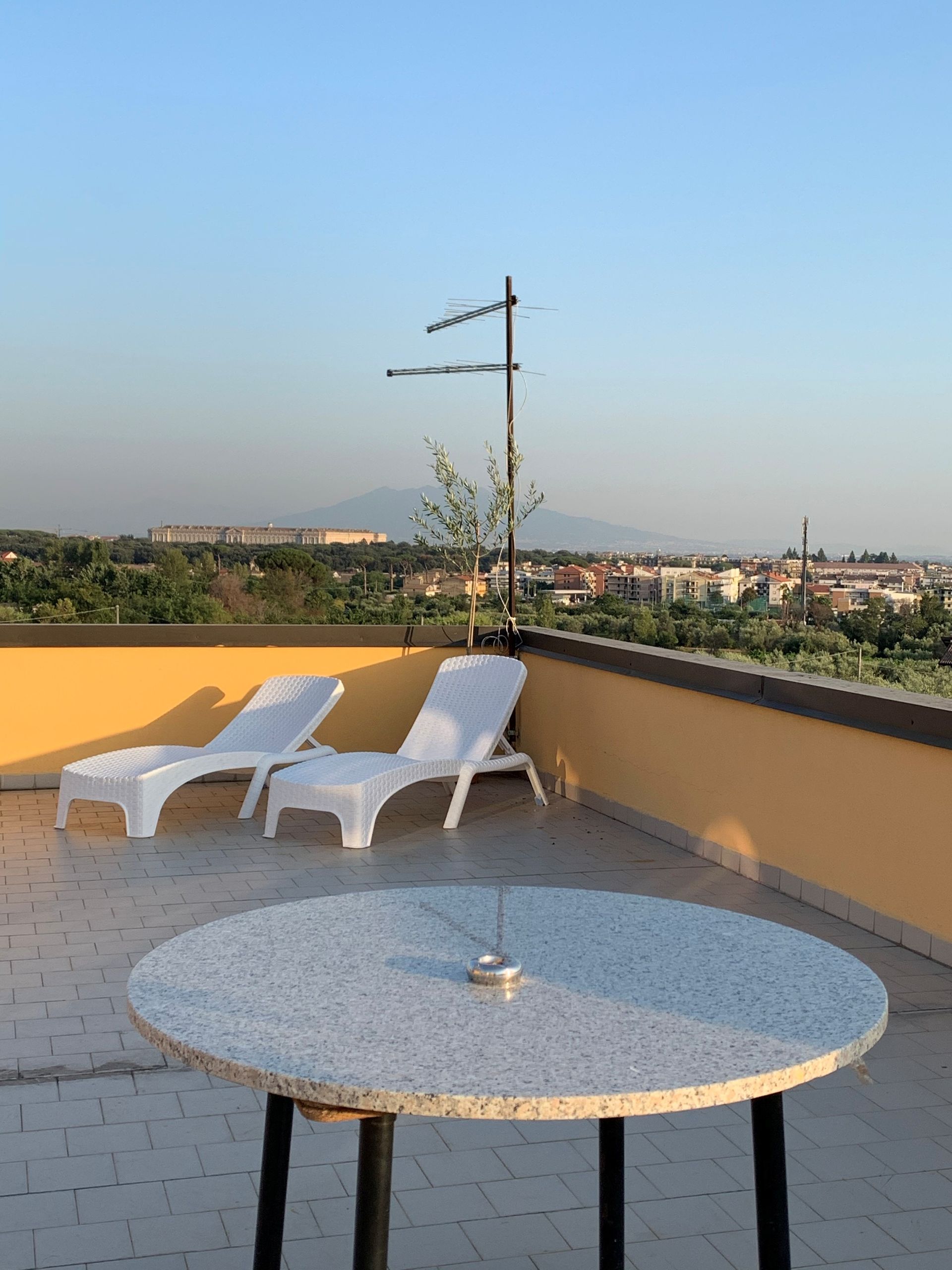Terrazza sul tetto con lettini bianchi, tavolo rotondo e vista sulla città al tramonto.