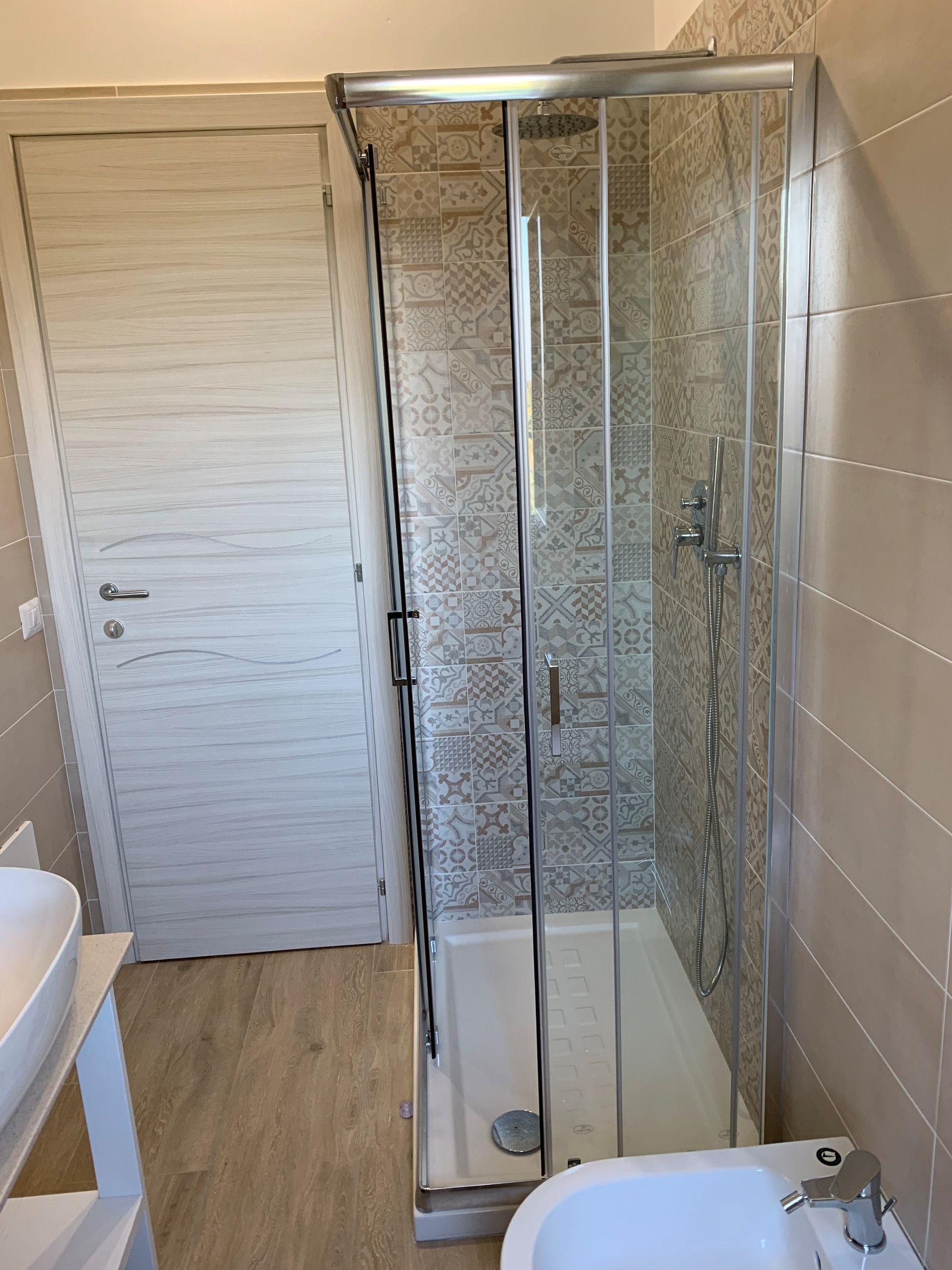 Bagno con porta a persiana bianca, box doccia in vetro e vasca da bagno freestanding.