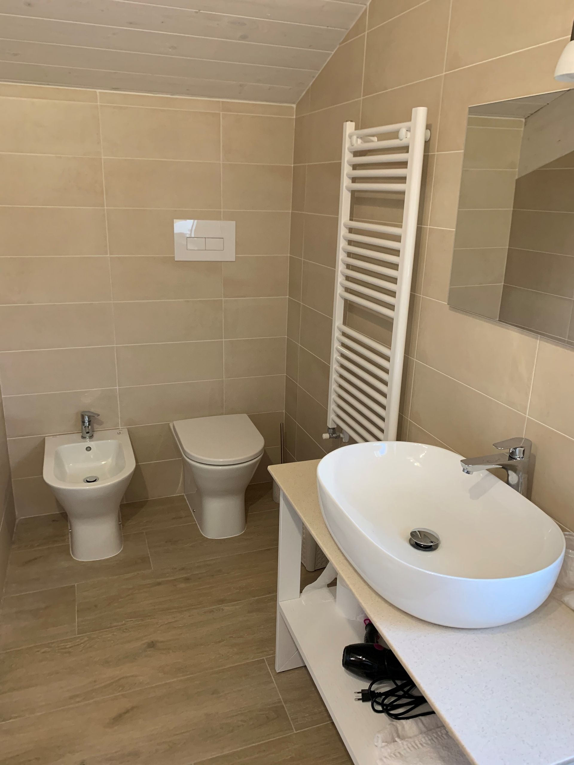 Bagno luminoso piastrellato con lavabo, WC, bidet e termoarredo bianco.