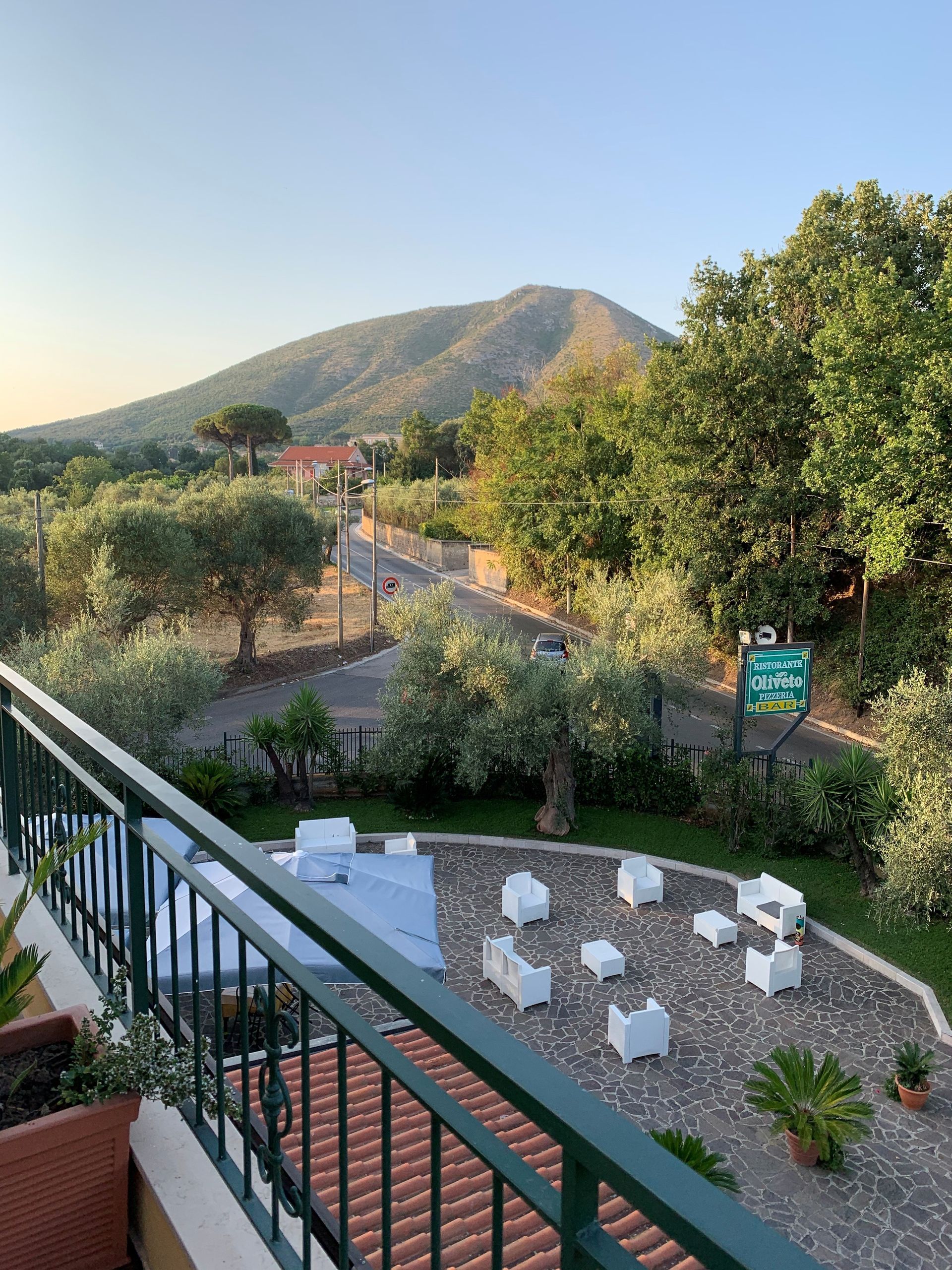 Giardino sul patio con sedie bianche, alberi verdi e una montagna in lontananza al tramonto.