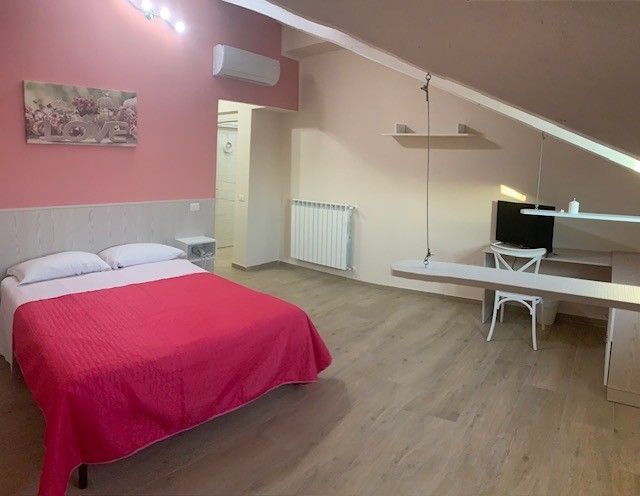 Accogliente camera da letto in mansarda con pareti rosa, copriletto rosso, scrivania, sedia e soffitto inclinato.