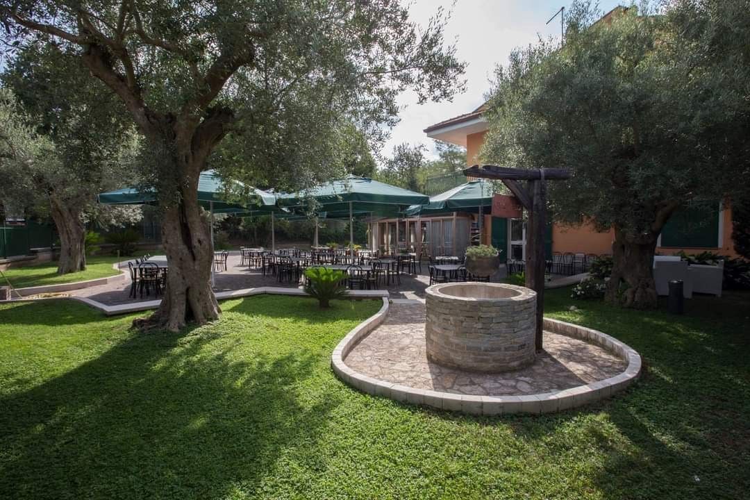 Cortile ombreggiato con alberi, fioriera circolare in pietra e posti a sedere all'aperto vicino a un edificio