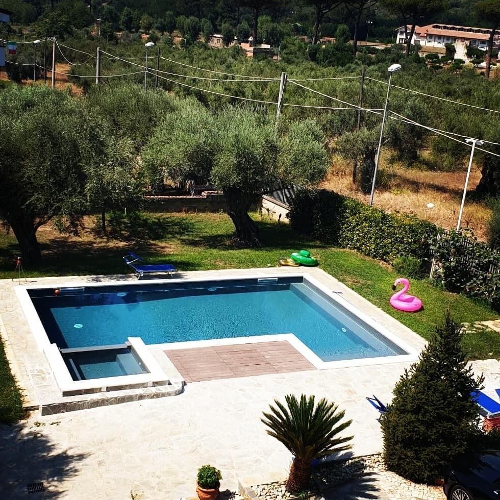 Piscina esterna in giardino con vasca rettangolare blu, sedie a sdraio e un fenicottero gonfiabile rosa in un angolo.