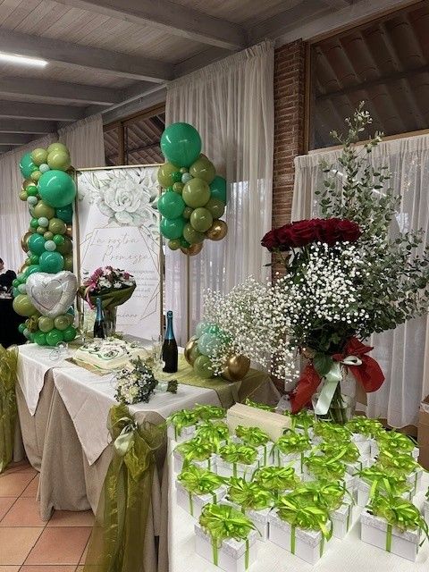 Tavolo da banchetto decorato con palloncini verdi e dorati, fiori e regali incartati per una festa al chiuso.