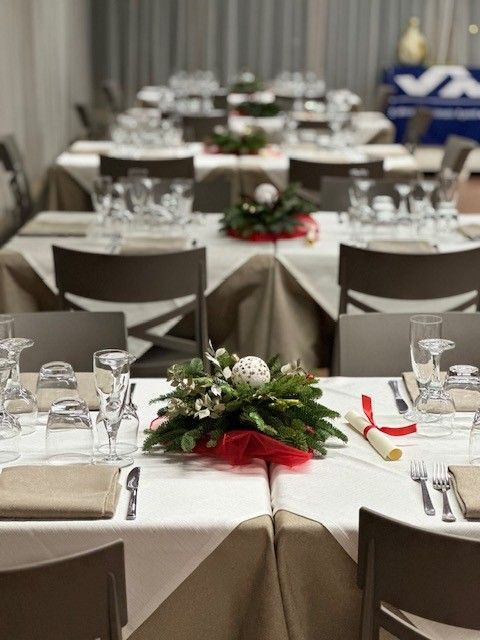 Allestire i tavoli del banchetto in una sala ricevimenti con tovaglie bianche, bicchieri e centrotavola floreali rossi e bianchi.