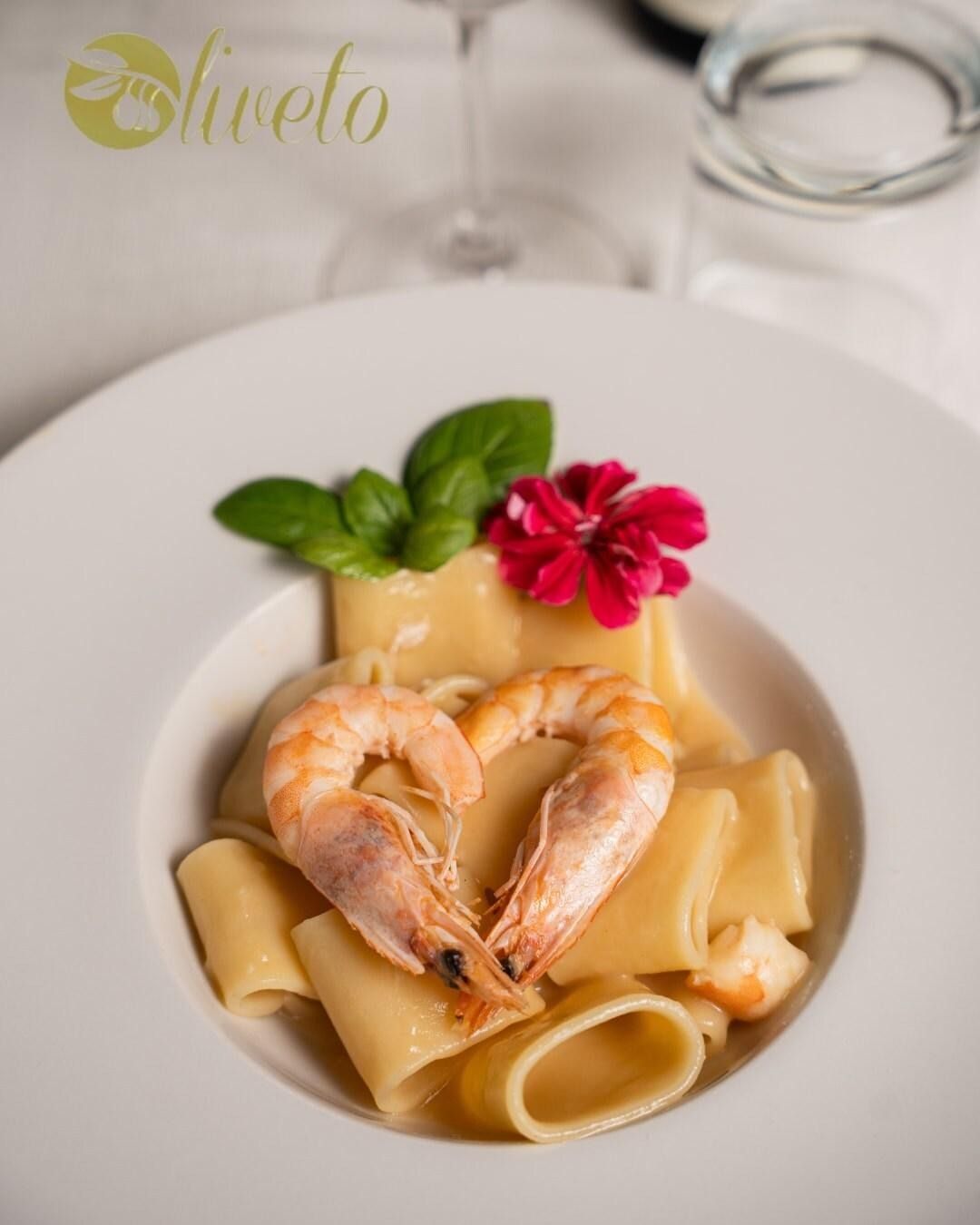 Pasta con gamberi in una ciotola bianca, guarnita con basilico e un fiore rosso su una tavola apparecchiata