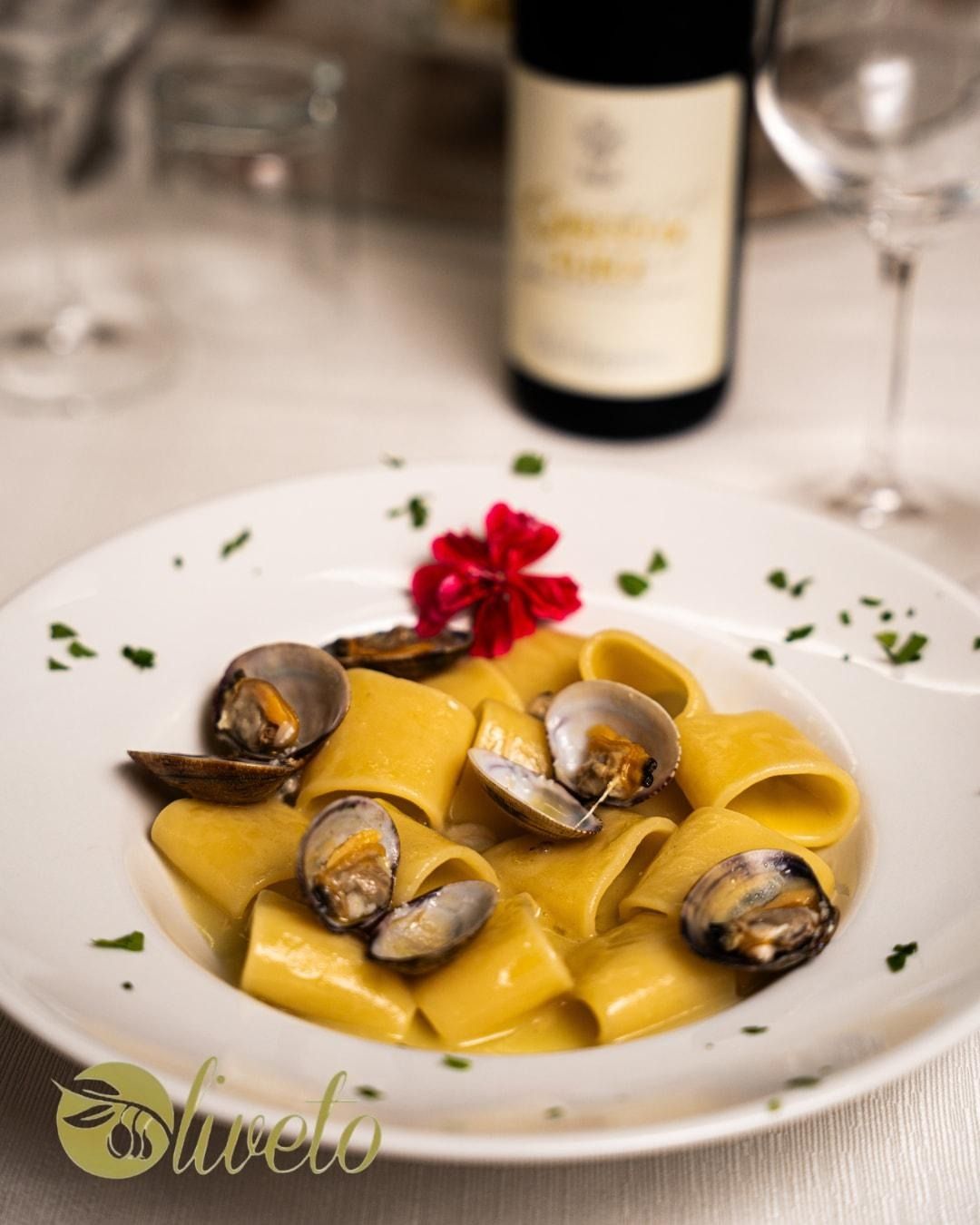 Pasta al nero di seppia con cozze, guarnita con erbe aromatiche e un fiore rosso su una tovaglia bianca.