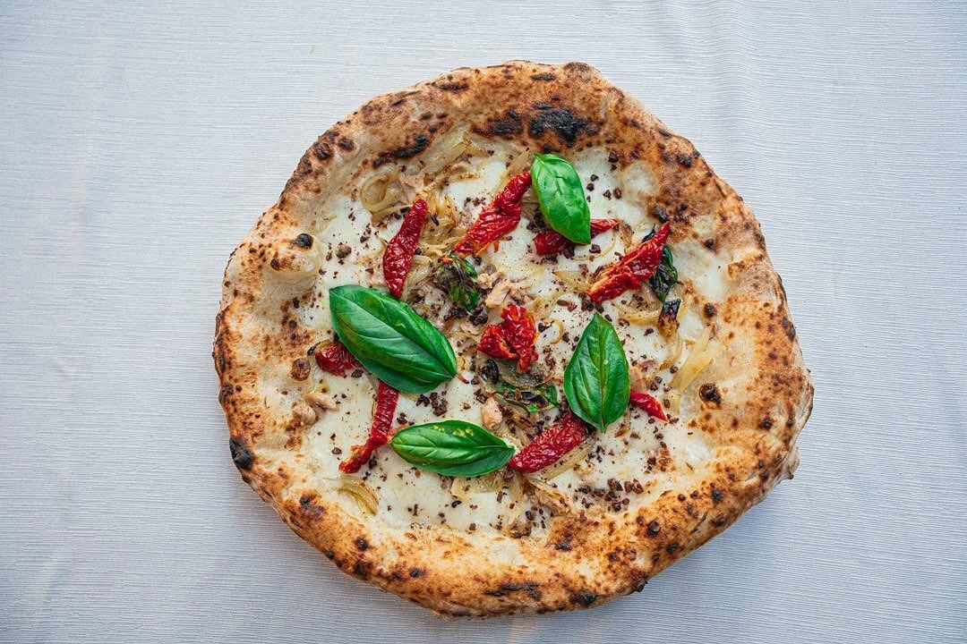 Pizza rustica con foglie di basilico, fette di pomodoro e formaggio fuso su una superficie grigia