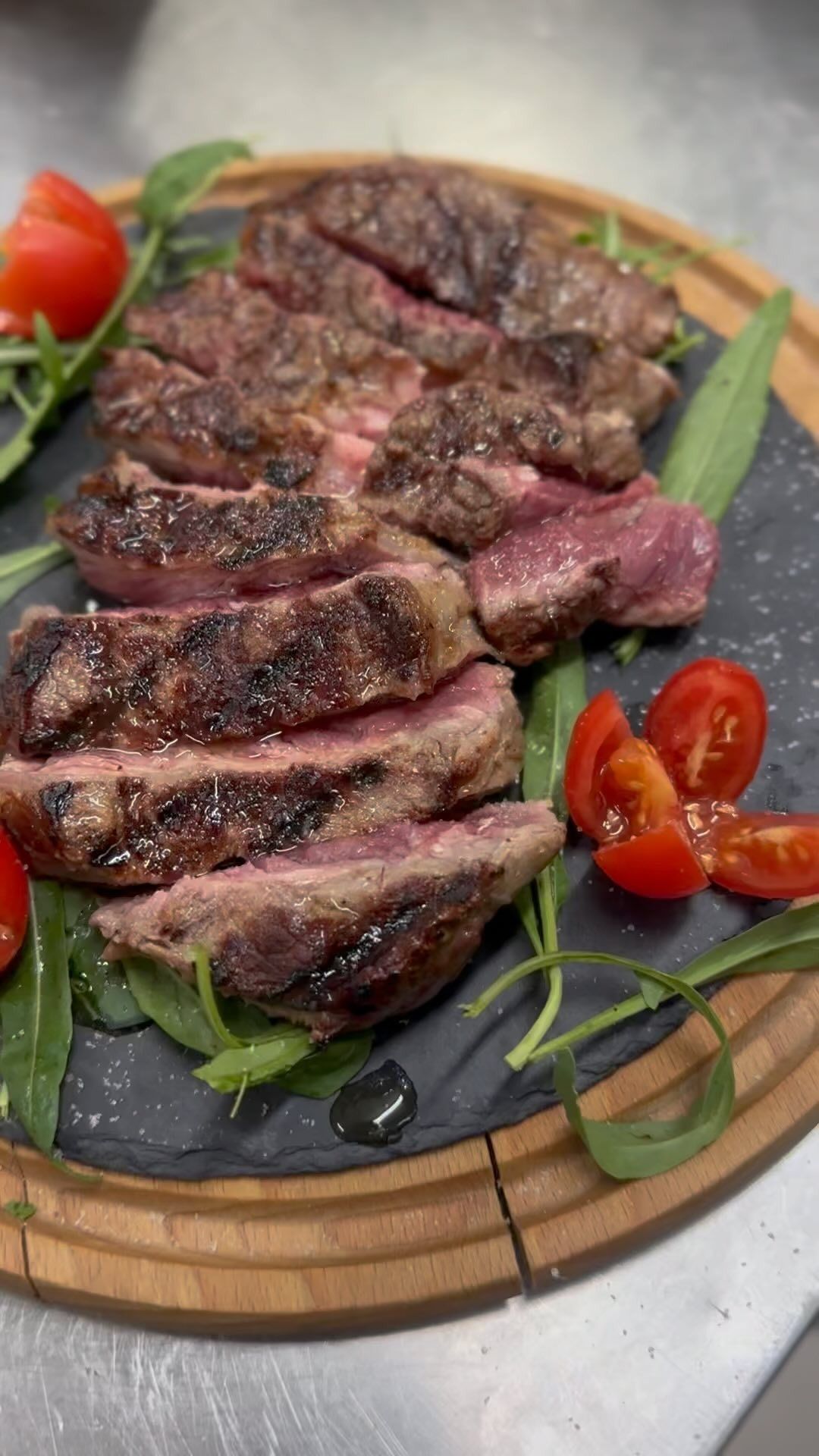 Fettine di bistecca al sangue servite su un tagliere di legno con pomodori e guarnizione verde.
