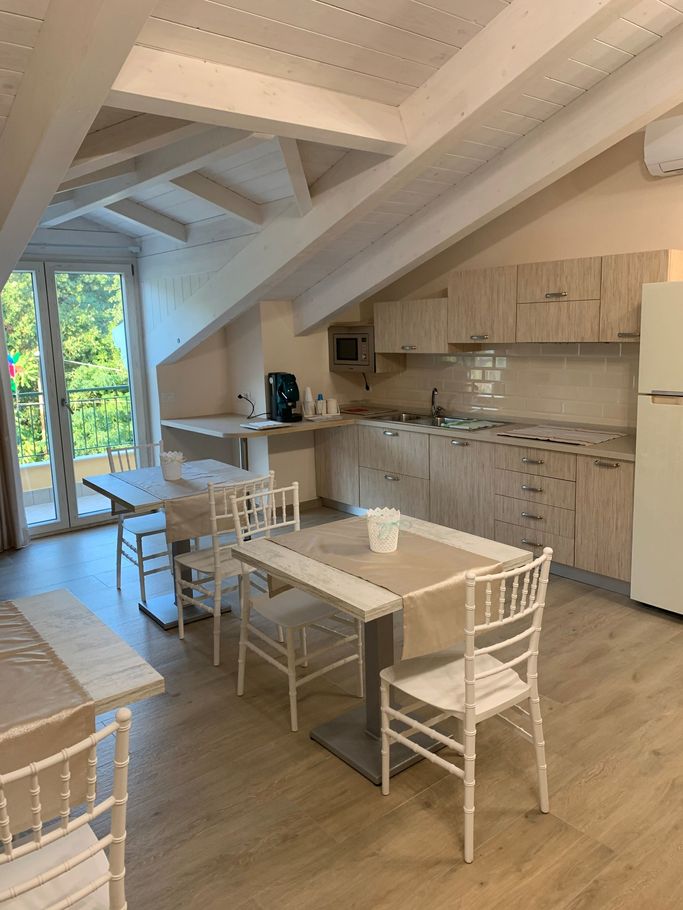 Luminosa cucina-sala da pranzo con travi bianche, tavolo, sedie e armadi in legno in un moderno spazio in stile loft.