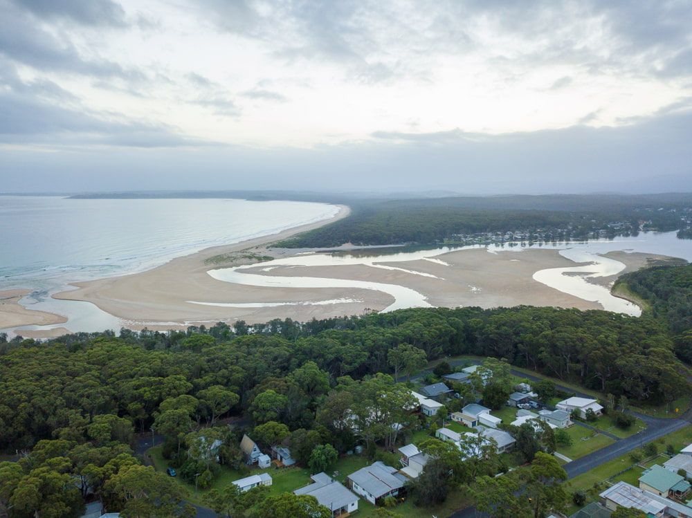 An Aerial View Of A Beach Surrounded By Trees And Houses — Johnson's Timber Agencies In Manyana, NSW