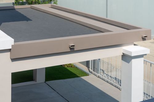 Modern patio pergola with beige frame, dark roof panels, and white support posts beside a driveway