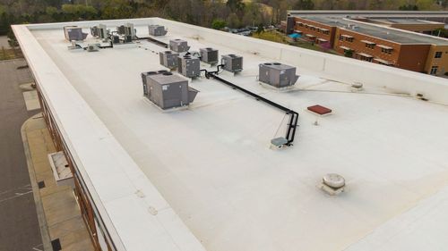 Rooftop with multiple HVAC units on a white commercial building, viewed from above.