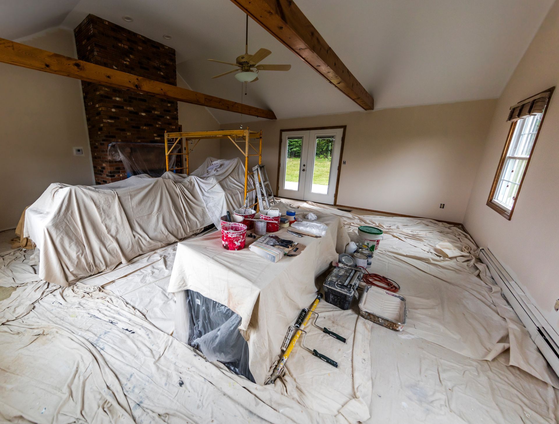 Pièce en rénovation, meubles et sol recouverts, matériel de peinture visible, aménagement intérieur.