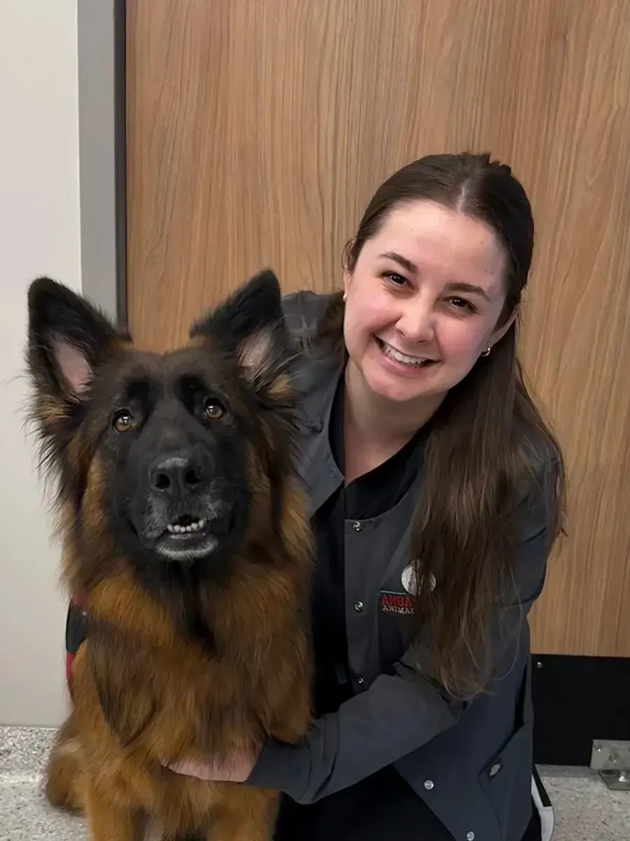 Woman sits beside a large gray-and-white dog in a pet store aisle.