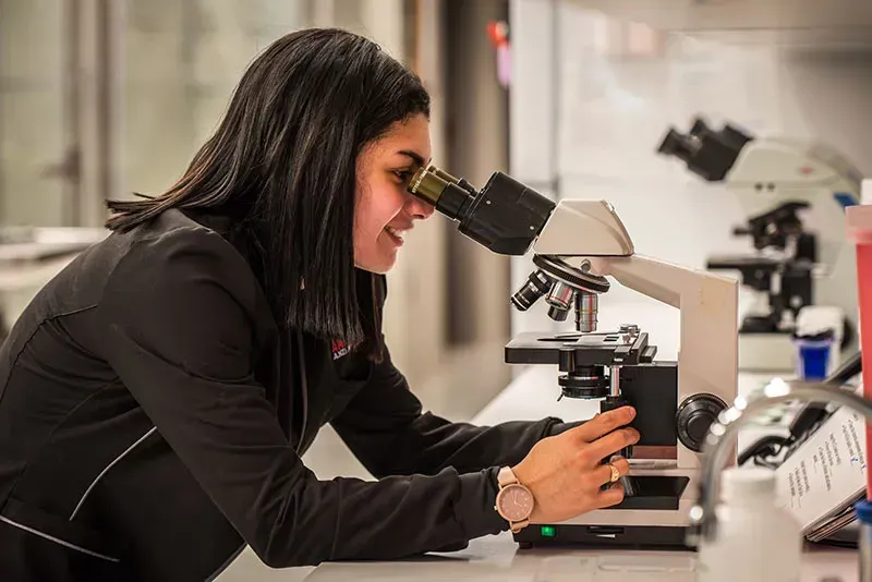 Woman using a microscope in a lab, focused on a sample.