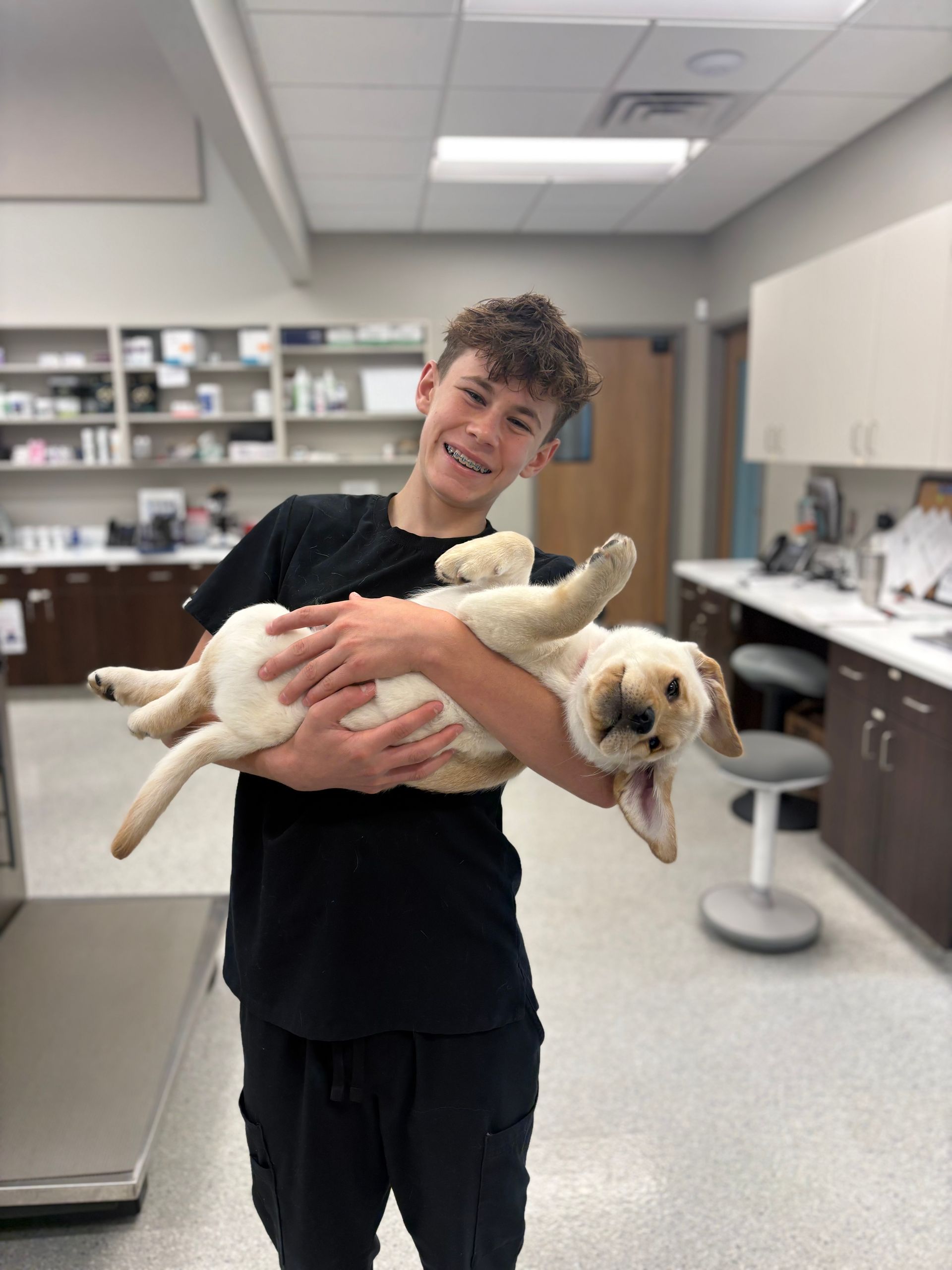 Woman kneels and hugs a large fluffy dog in a clinic hallway.