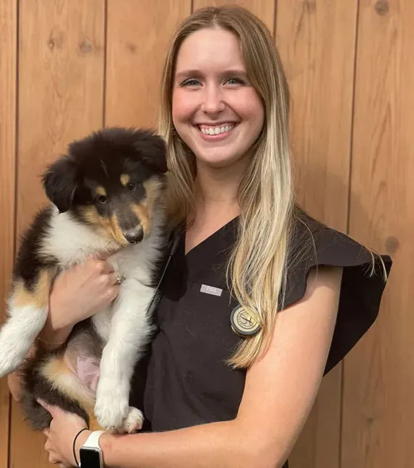 Woman smiling and holding a black-and-tan puppy against a wooden wall