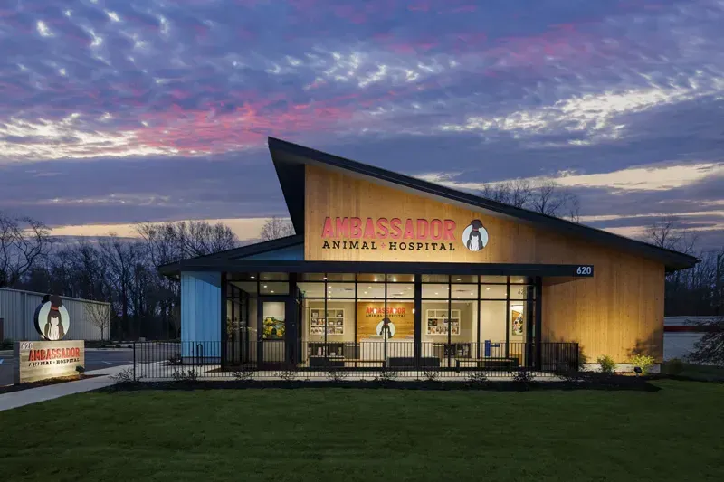 Modern storefront at dusk with warm-lit windows and a colorful sunset sky