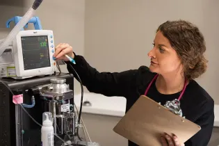 Technician adjusting a medical machine while holding a clipboard in a clinical setting